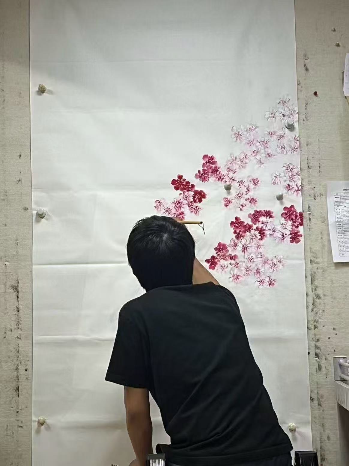 Person painting floral designs on a large white canvas with pink and red flowers.